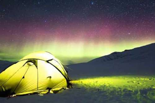 A glowing yellow tent in a snowy landscape under a vibrant aurora borealis and starry night sky.