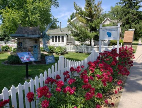 A charming garden with vibrant flowers, a windmill, and a sign for "Nason's Picture Gardens" in a sunny setting.
