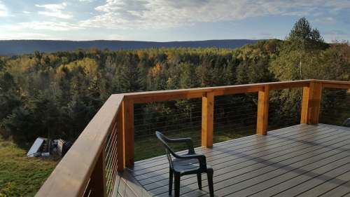 A wooden deck overlooks a forested landscape with autumn foliage and a single chair in the foreground.