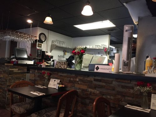 Cozy restaurant interior with a stone counter, tables set for dining, and a kitchen visible in the background.