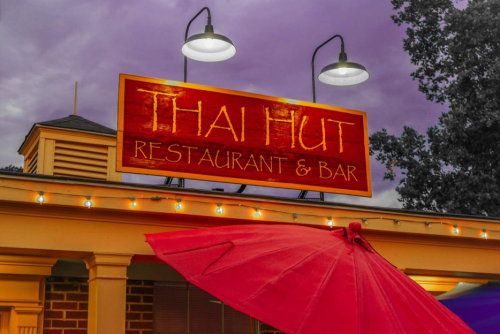 Sign for "Thai Hut Restaurant & Bar" with an umbrella in front, set against a cloudy sky.