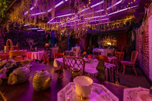 A whimsical dining space adorned with colorful lights, floral decor, and elegantly set tables.