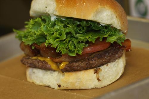 A close-up of a burger with a beef patty, melted cheese, bacon, lettuce, and tomato on a soft bun.