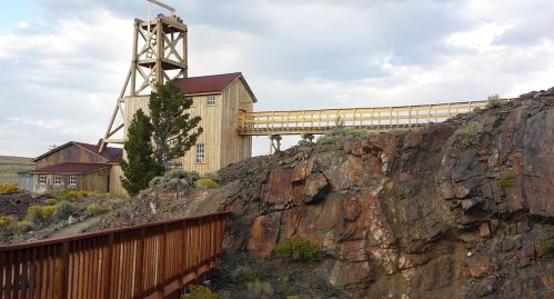 A wooden structure resembling a mining facility sits on rocky terrain under a cloudy sky.
