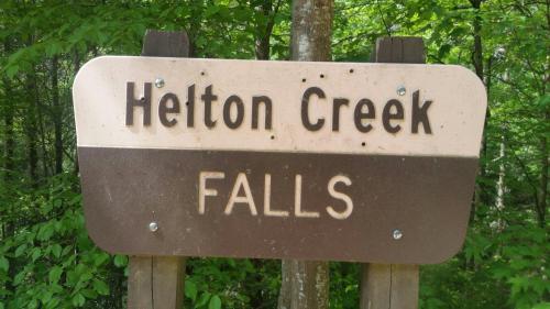Sign for Helton Creek Falls, featuring green foliage in the background.