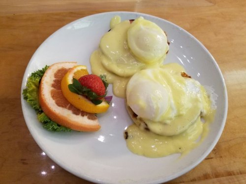 A plate of eggs Benedict topped with hollandaise sauce, served with a side of fresh fruit and greens.