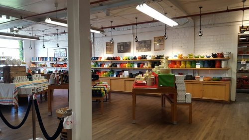 Brightly lit store interior featuring shelves of colorful dishware and kitchen items, with wooden tables and a welcoming atmosphere.