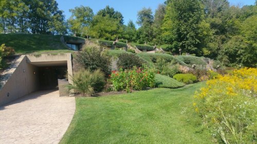 A landscaped garden with colorful flowers and greenery, leading to a modern building partially embedded in a hillside.