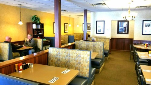A cozy diner interior with booths and tables, featuring two men chatting at a table and warm lighting.