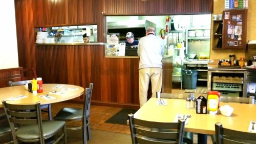 A cozy diner interior with tables set for dining and staff working in the kitchen behind a counter.