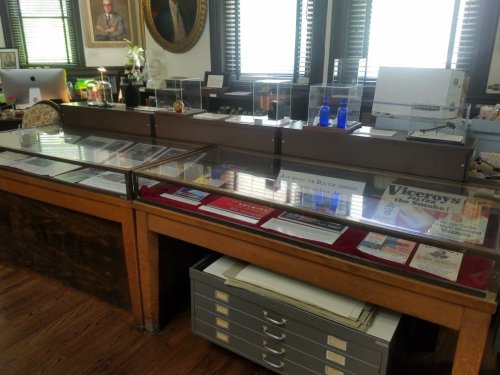 Display cases with historical documents and artifacts in a well-lit room, featuring a portrait on the wall.