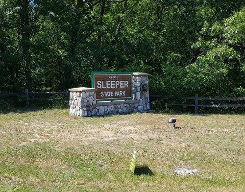 Sign for Albert E. Sleeper State Park, surrounded by trees and grass, with a stone base and wooden elements.