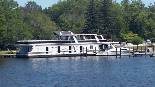 Two boats docked by a lush green shoreline, with trees in the background and a clear blue sky above.