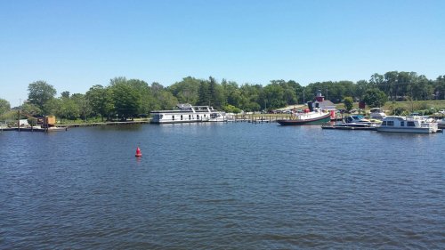 A calm lake scene with boats docked, surrounded by greenery and a clear blue sky.