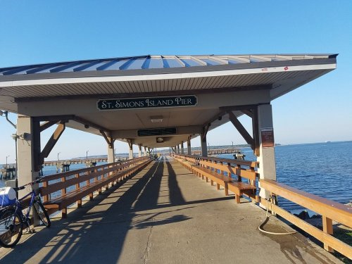 View of St. Simons Island Pier with wooden walkway, railings, and a clear blue sky over the water.