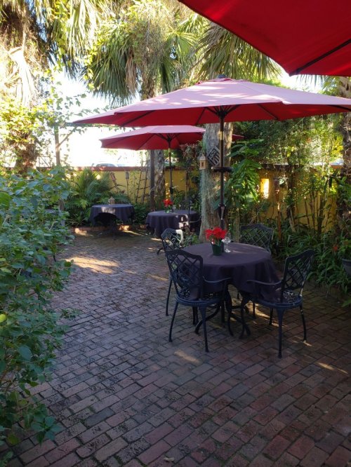 Outdoor dining area with tables under red umbrellas, surrounded by greenery and tropical plants.