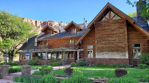 A rustic wooden lodge surrounded by greenery and mountains under a clear blue sky.