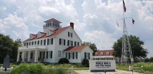 Historic white building with red roof, featuring a museum sign for the World War II Home Front Museum, under a cloudy sky.