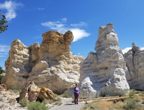 A person stands near large, colorful rock formations under a bright blue sky with scattered clouds.