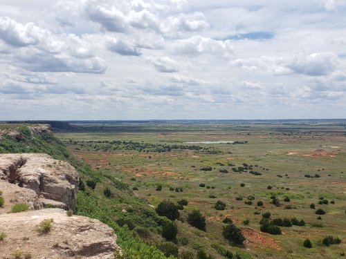 A vast landscape with rolling hills, green fields, and scattered clouds under a blue sky.
