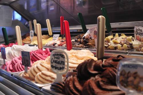 A colorful display of various gelato flavors in a shop, with scoops arranged in metal containers and labels.