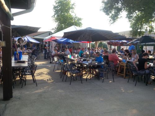 Outdoor dining area filled with people at tables under umbrellas, enjoying a sunny day.