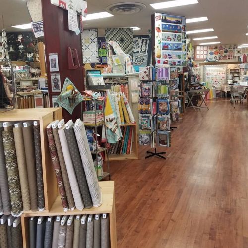 A fabric store interior with shelves of colorful fabrics, quilting supplies, and a wooden floor.