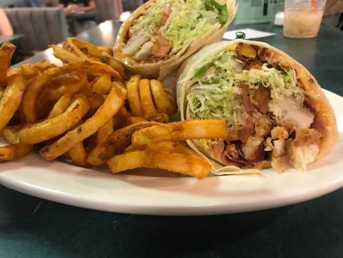 A plate with two wraps filled with chicken and lettuce, accompanied by a side of curly fries.