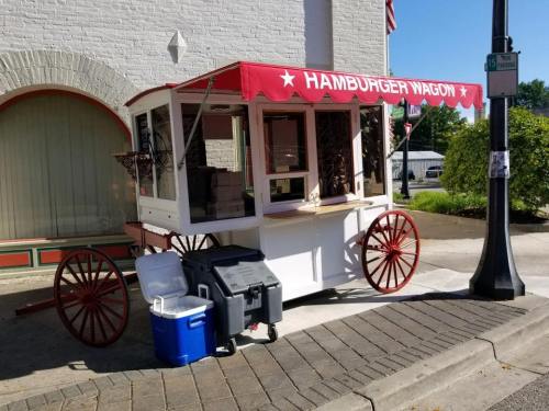 A vintage-style hamburger wagon with a red canopy, parked on a sidewalk near a building.
