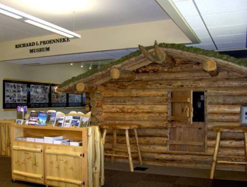 Log cabin display inside the Richard L. Proenneke Museum, with informational panels and wooden furniture.