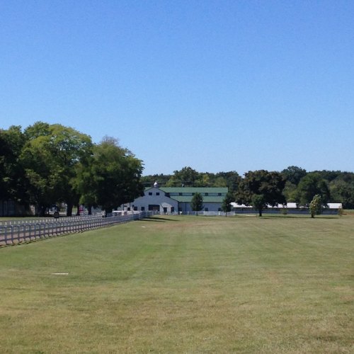 A clear blue sky over a grassy field leading to a white barn and trees in the background.