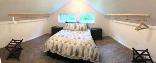 Cozy attic bedroom with a bed, two nightstands, and hanging space for clothes under sloped ceilings.