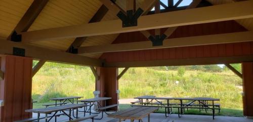 A spacious pavilion with wooden beams and picnic tables, surrounded by greenery and open fields.