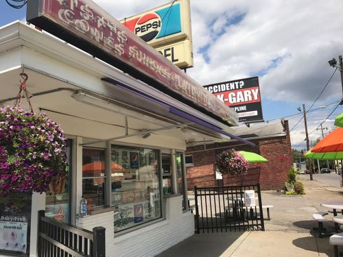 A colorful ice cream shop with hanging flower baskets and outdoor seating under umbrellas on a sunny day.