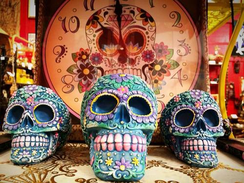 Three colorful decorative skulls with floral designs, set against a vibrant background featuring a sugar skull motif.