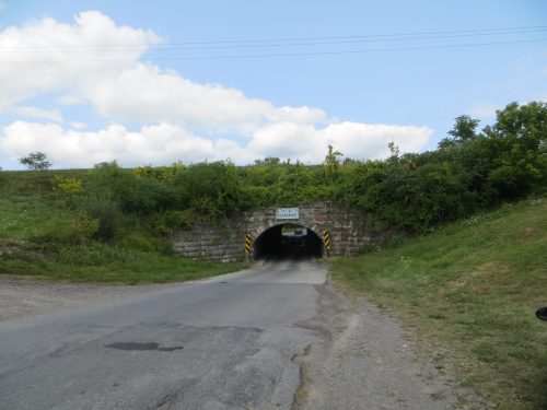 A road leading to a dark tunnel, surrounded by greenery and a sign indicating the tunnel's name.
