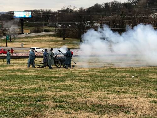 Civil war reenactors firing a cannon, with smoke billowing in a grassy field.