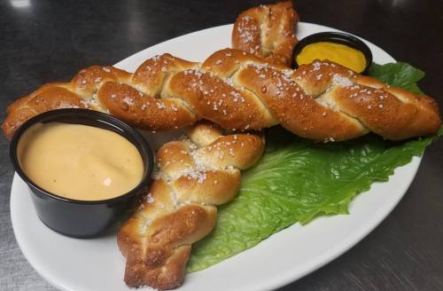 A plate of twisted pretzels with coarse salt, served with mustard and a creamy dipping sauce on a bed of lettuce.
