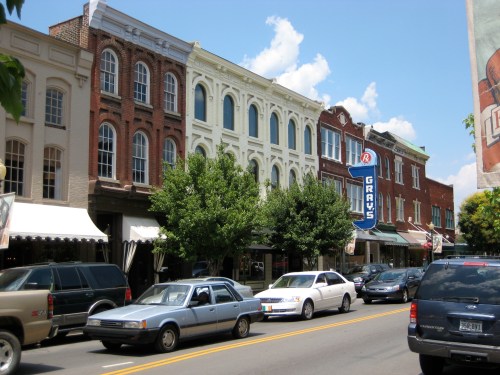 Historic buildings line a street with trees and parked cars, featuring a prominent sign for "Grays."