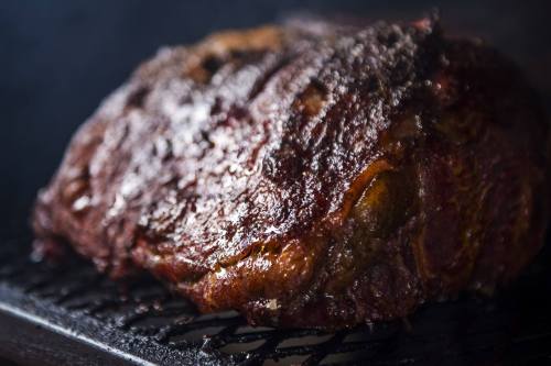 A close-up of a perfectly smoked, juicy piece of meat resting on a grill, showcasing a rich, caramelized crust.