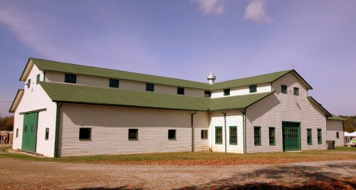 A large white barn with a green roof, featuring multiple windows and a double door, set against a clear blue sky.
