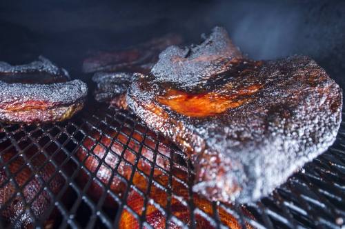 Close-up of smoky, charred meat on a grill, showcasing a rich, dark crust and juicy texture.