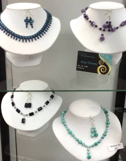 Display of four elegant jewelry sets on busts, featuring necklaces and earrings in various colors and styles.