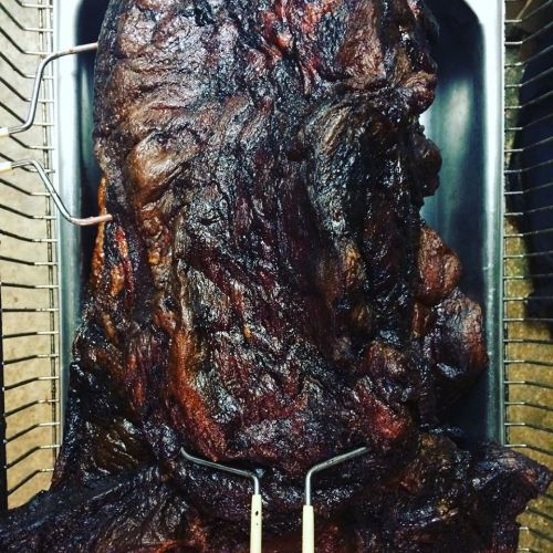A large, smoked piece of meat resting in a tray, showcasing a dark, charred exterior.