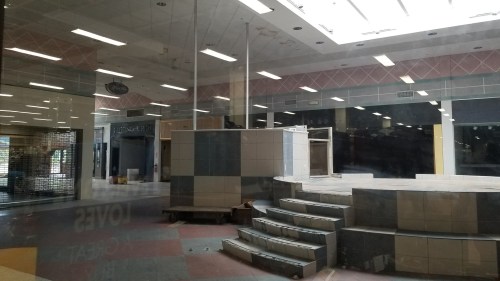 Abandoned indoor space with a tiled platform and steps, visible through a glass window.