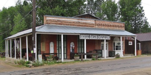 Historic brick building with a metal roof, featuring a sign for the Boise Basin Museum, surrounded by trees.