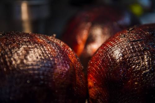 Close-up of three shiny, dark, charred fruits with textured skin, glistening under soft light.
