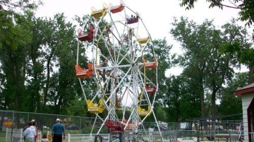 A colorful Ferris wheel at a fair, surrounded by trees and people enjoying the ride.