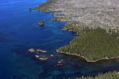 Aerial view of a blue lake surrounded by forested land and rocky shorelines, with scattered islands visible.