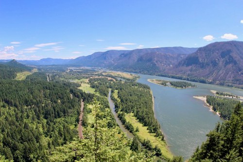 A panoramic view of a river winding through lush green forests and mountains under a clear blue sky.